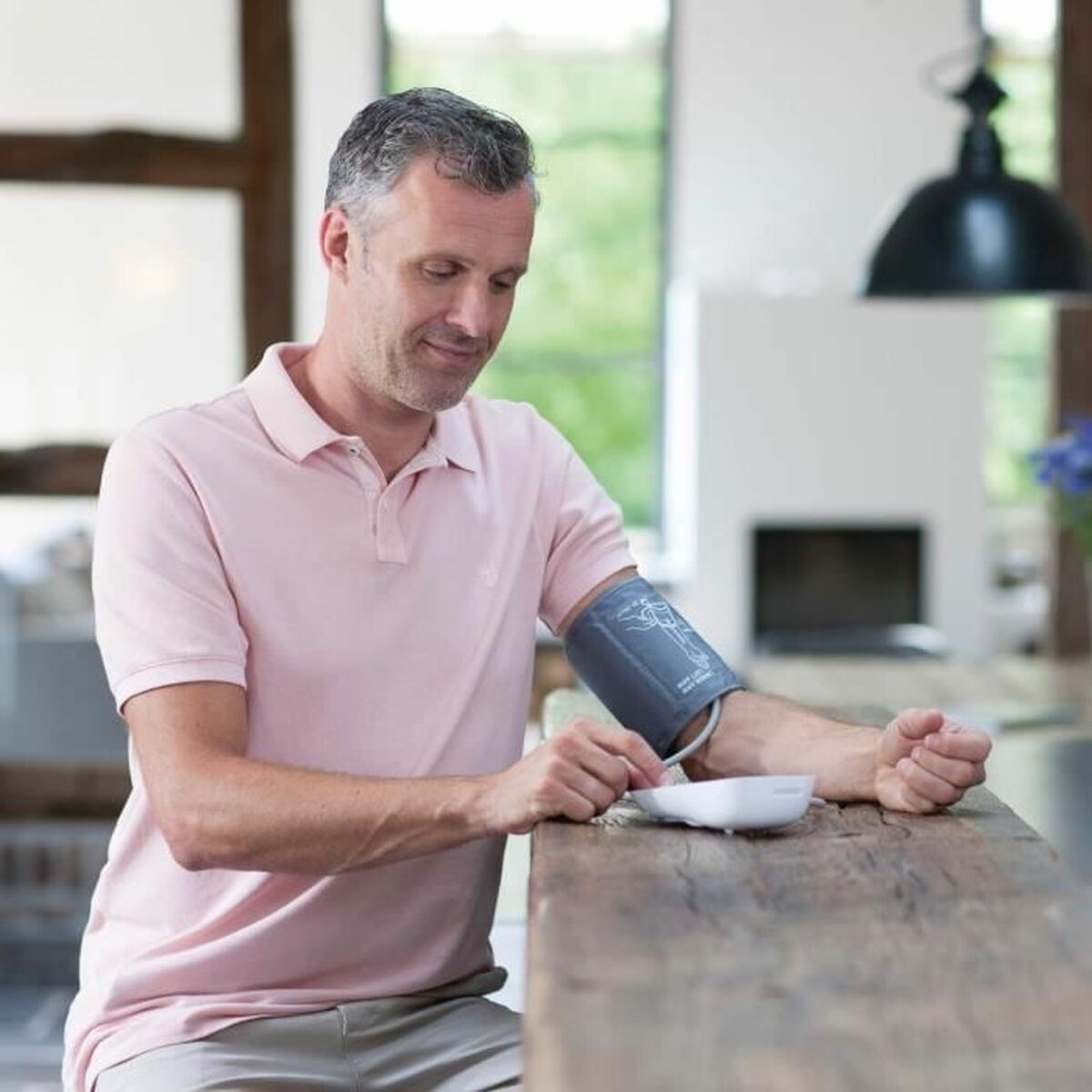 Hombre usando un tensiómetro de brazo Medisana en casa para controlar su presión arterial.