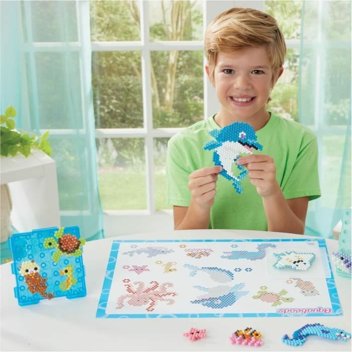 Niño sonriente sosteniendo un delfín hecho con Mosaico Aquabeads multicolor infantil, disfrutando de su actividad creativa.