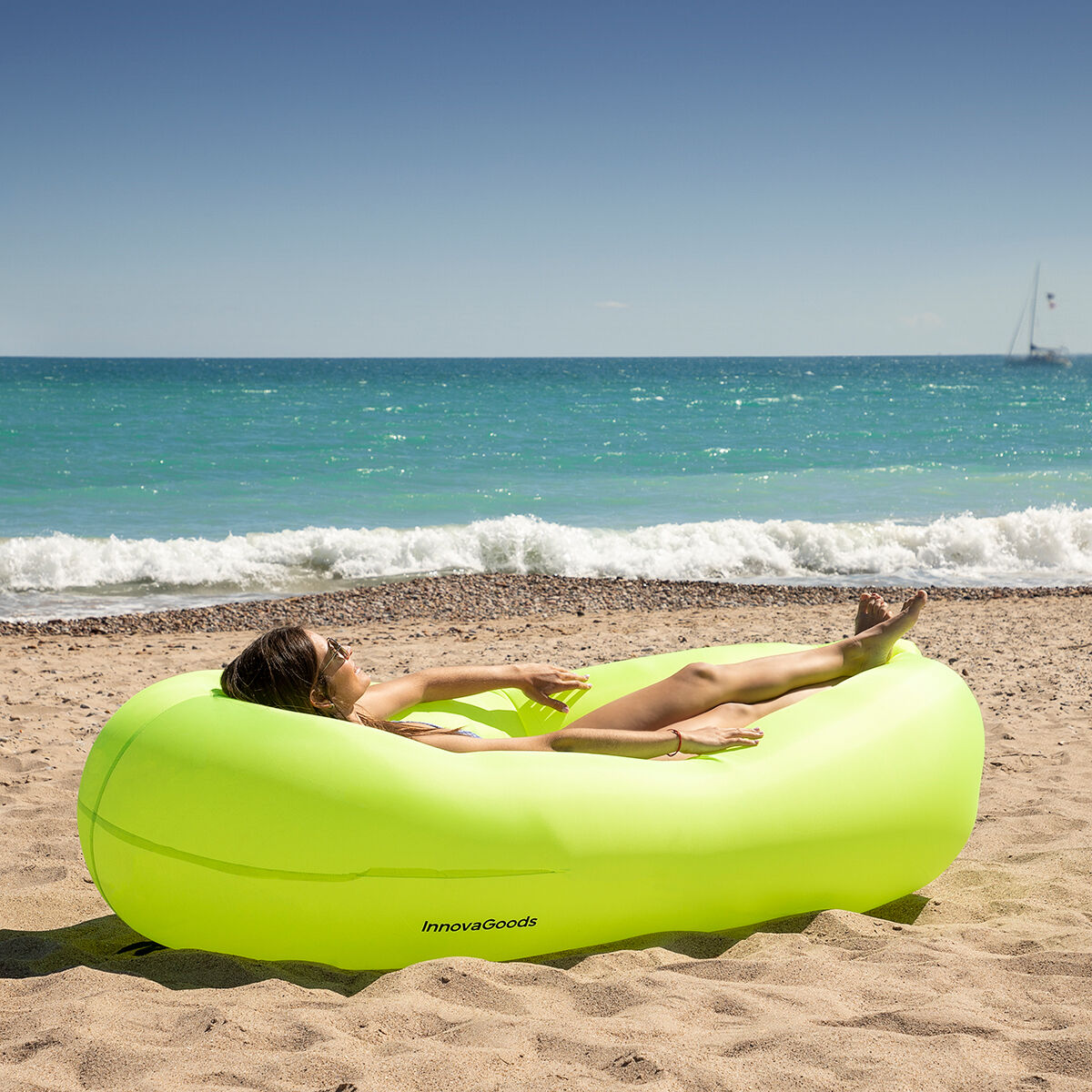 Mujer relajándose en un sofá hinchable InnovaGoods en la playa, disfrutando del sol y el mar