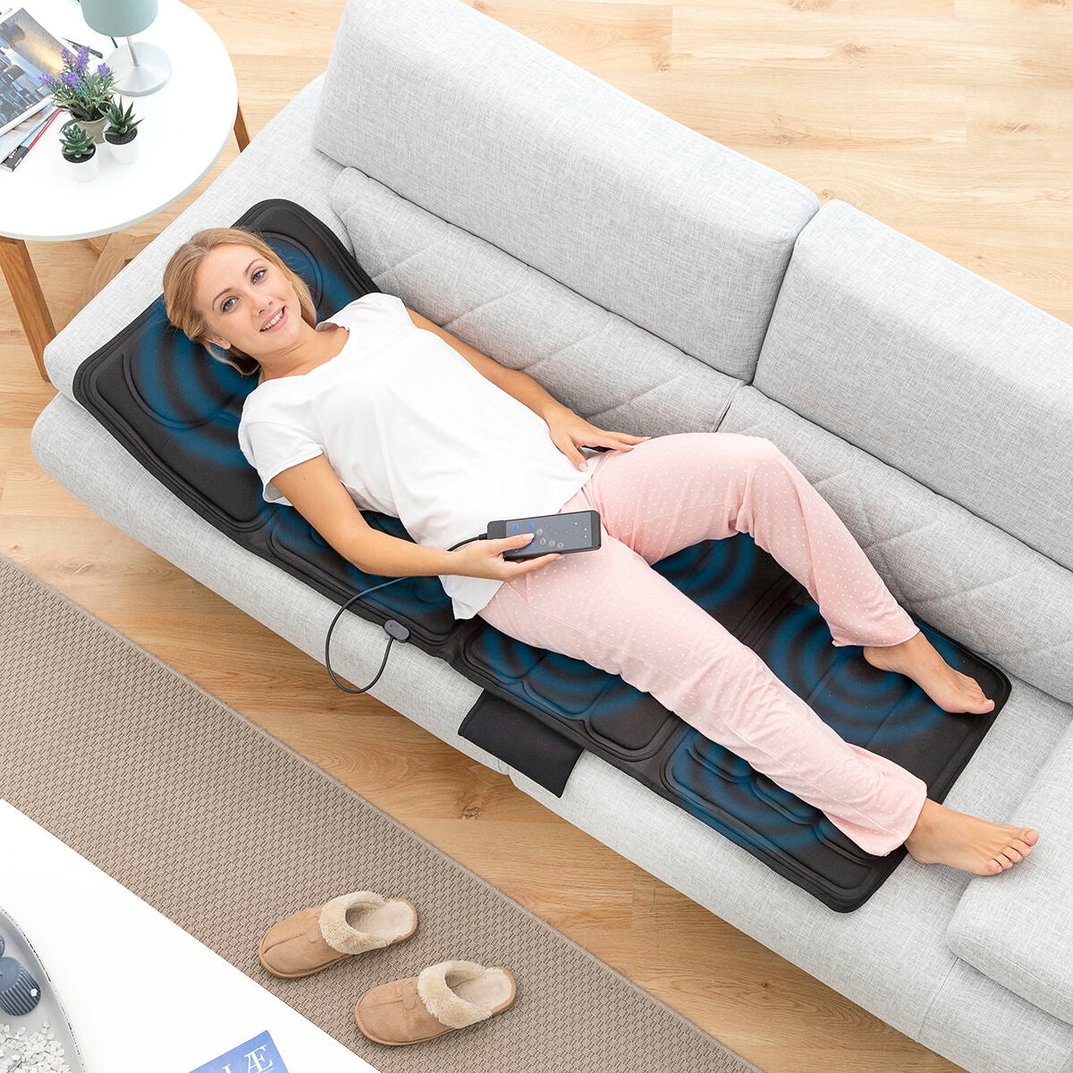 Esterilla de masaje corporal InnovaGoods en uso, mujer relajándose en el sofá con control remoto en la mano.