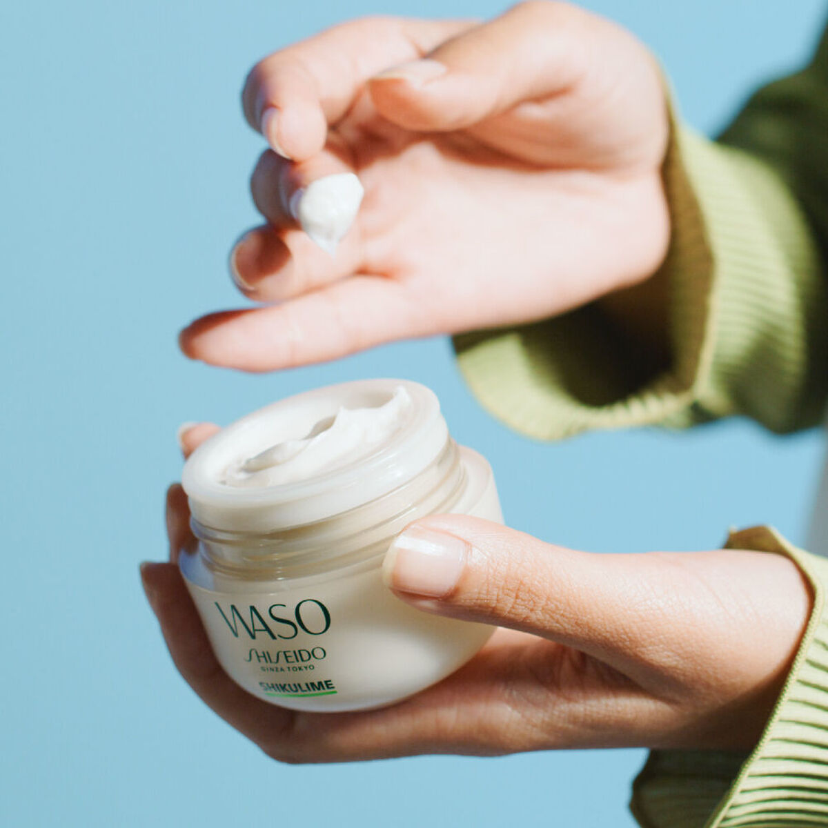 Shiseido WASO moisturizing cream being applied from a jar by a person with well-groomed hands.