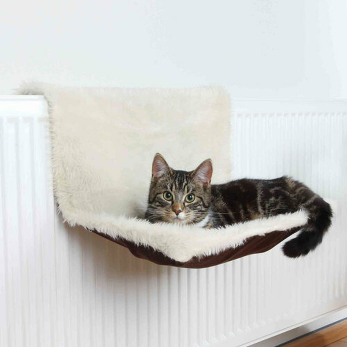 Cama para gato Trixie marrón crema con gato descansando sobre un radiador.