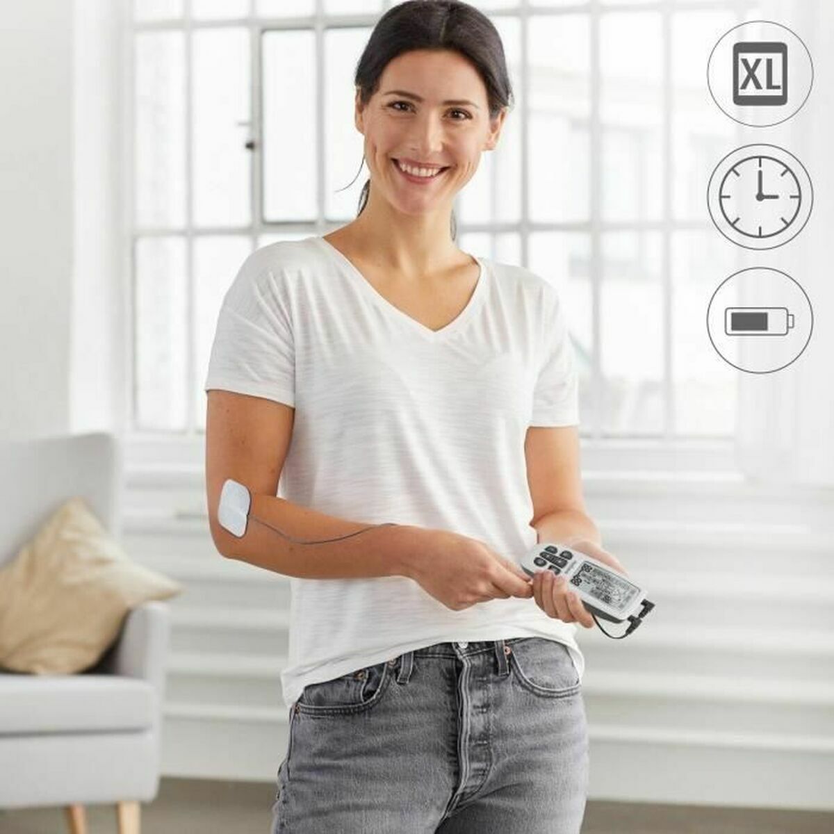 Mujer usando el electroestimulador muscular Medisana en el brazo mientras sonríe en un entorno hogareño.