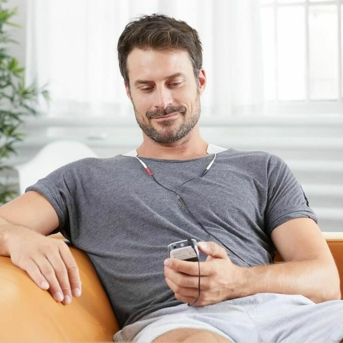 Hombre usando el electroestimulador muscular Medisana mientras escucha música en su celular.