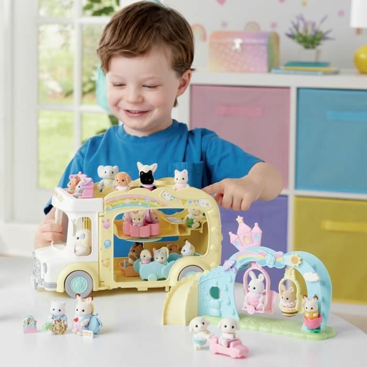 Niño jugando con accesorios para casa de muñecas Sylvanian Families, incluyendo un autobús y un parque de juegos.