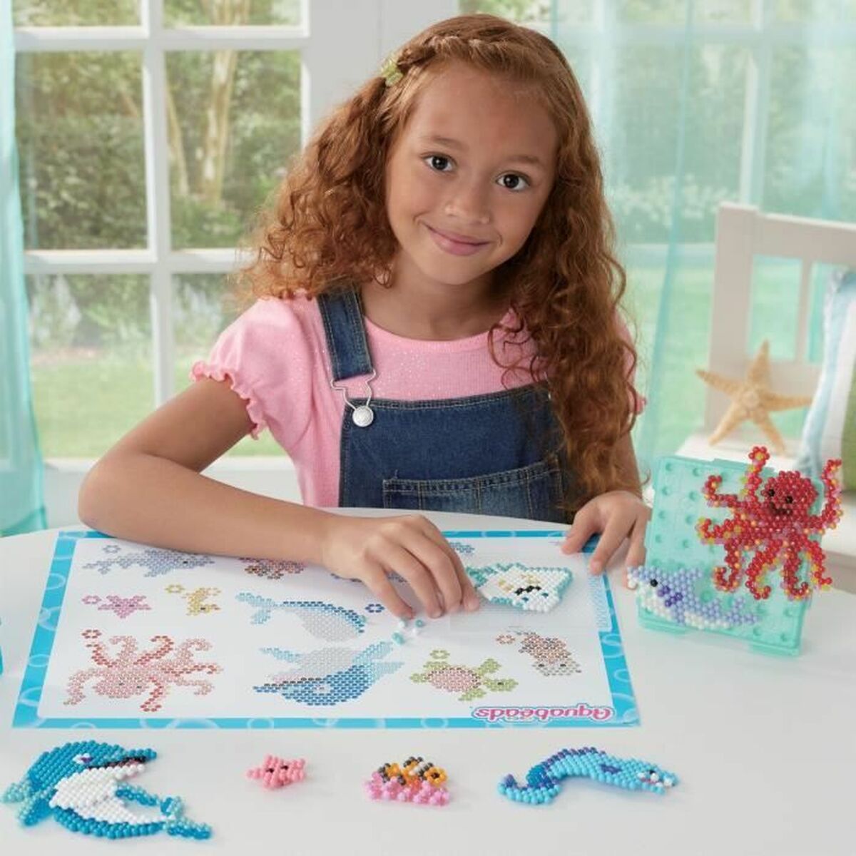 Niña feliz usando Mosaico Aquabeads multicolor infantil con diseño divertido alrededor.